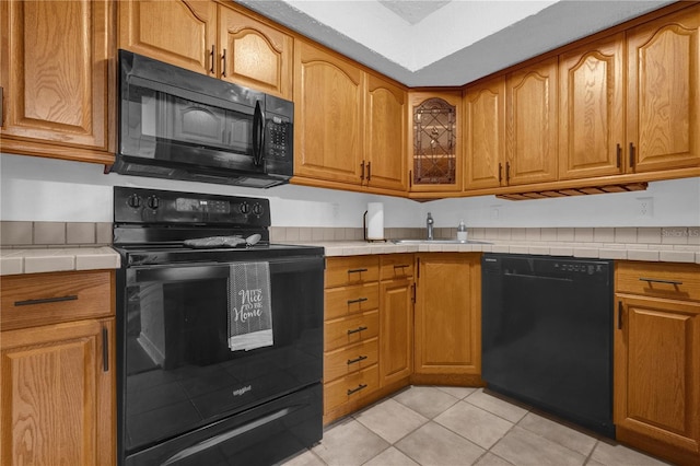 kitchen with black appliances, tile counters, light tile patterned floors, and sink