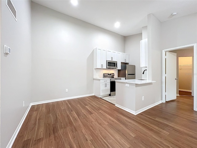 kitchen featuring appliances with stainless steel finishes, light hardwood / wood-style floors, kitchen peninsula, and white cabinetry