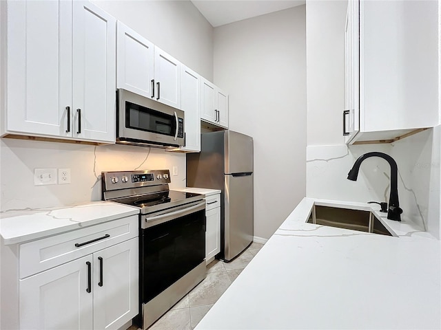 kitchen with light stone counters, light tile patterned floors, sink, white cabinetry, and appliances with stainless steel finishes