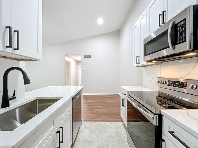 kitchen with sink, white cabinets, vaulted ceiling, stainless steel appliances, and light tile patterned floors