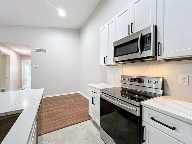 kitchen with white cabinets, appliances with stainless steel finishes, light wood-type flooring, and vaulted ceiling