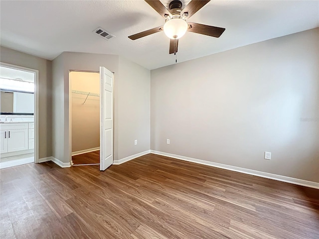 unfurnished bedroom with a closet, ceiling fan, a walk in closet, hardwood / wood-style flooring, and sink