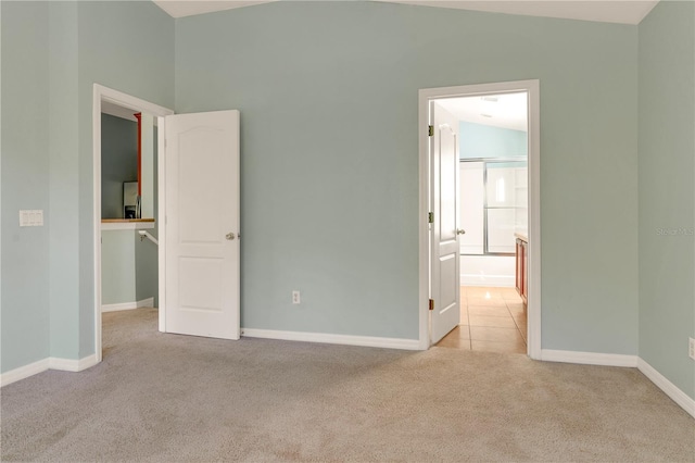 unfurnished bedroom with connected bathroom, light colored carpet, and lofted ceiling