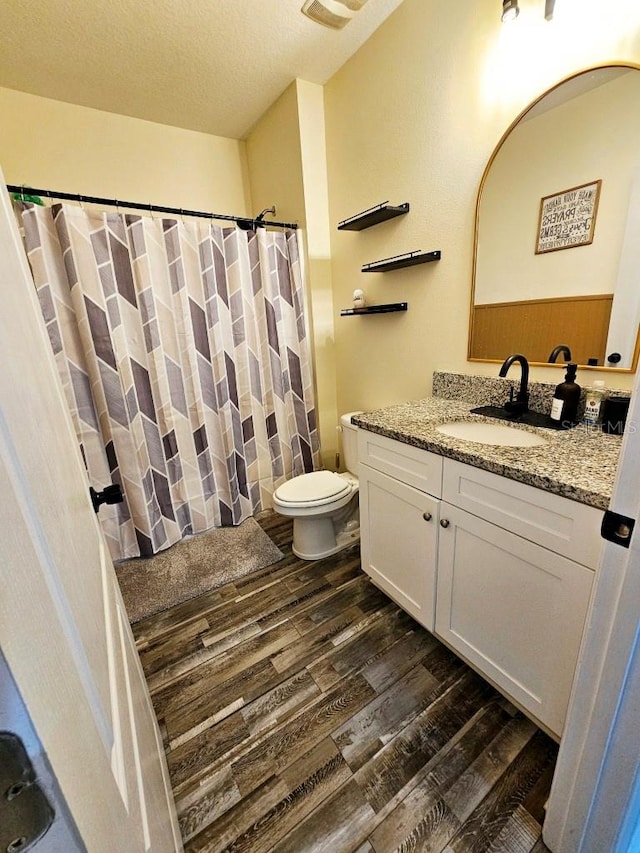 bathroom featuring a textured ceiling, hardwood / wood-style flooring, a shower with curtain, vanity, and toilet