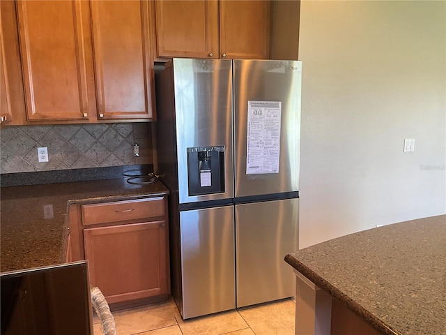 kitchen with decorative backsplash, dark stone countertops, stainless steel refrigerator with ice dispenser, and light tile patterned floors