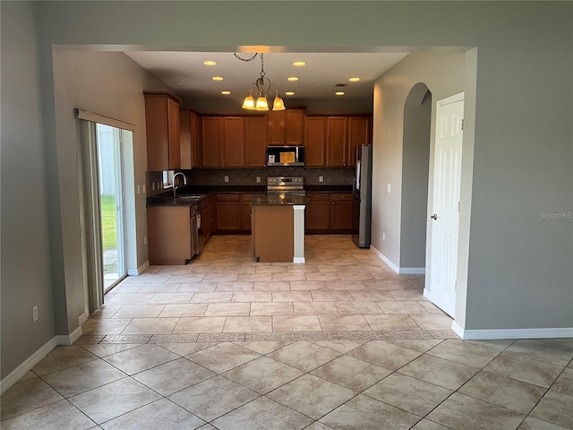 kitchen featuring appliances with stainless steel finishes, hanging light fixtures, decorative backsplash, a kitchen island, and sink