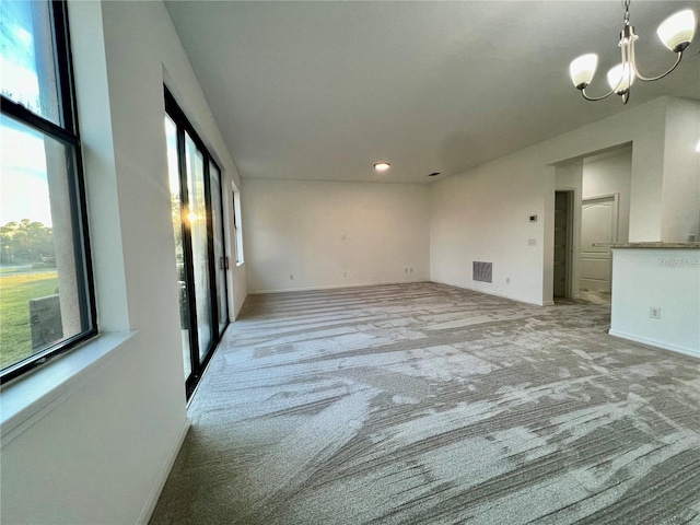 carpeted empty room with a notable chandelier and a wealth of natural light