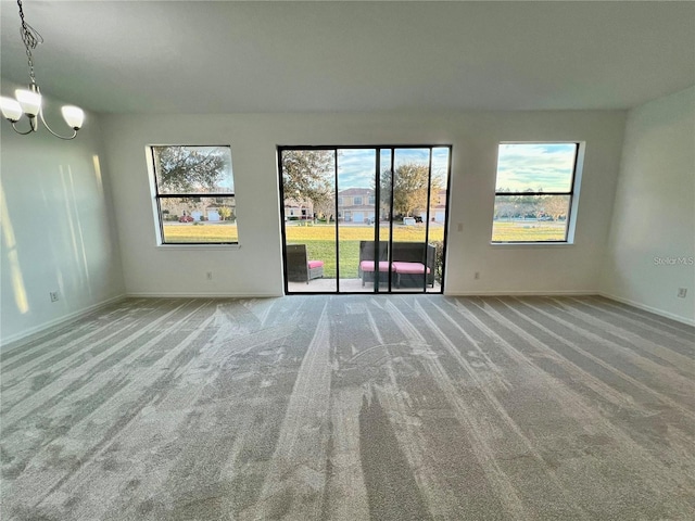 carpeted spare room with an inviting chandelier and a wealth of natural light