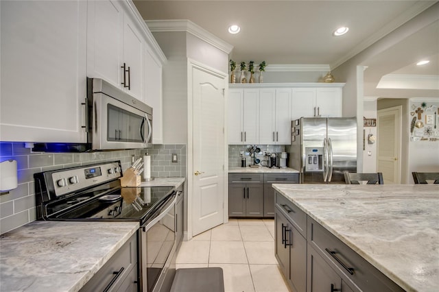 kitchen with ornamental molding, stainless steel appliances, white cabinetry, and light tile patterned flooring