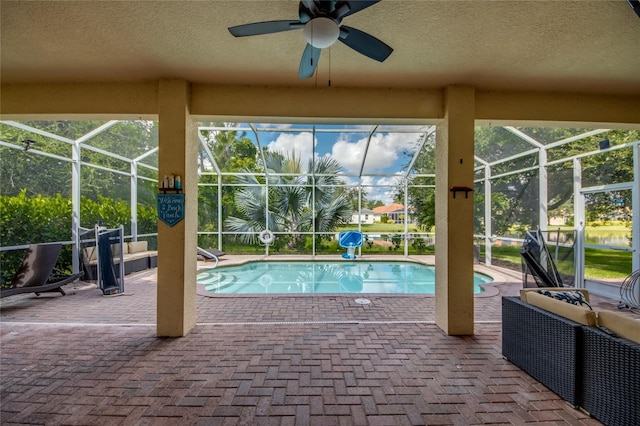 view of swimming pool featuring glass enclosure, ceiling fan, and a patio area