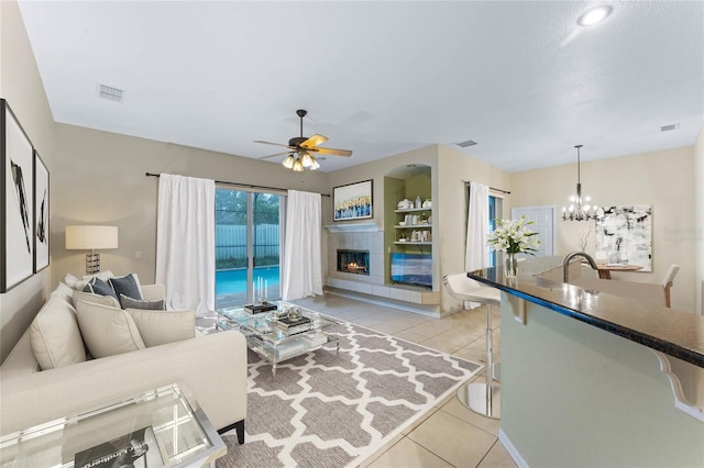 tiled living room with a tile fireplace and ceiling fan with notable chandelier