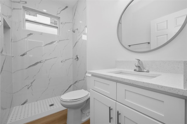 bathroom with toilet, vanity, wood-type flooring, and a tile shower