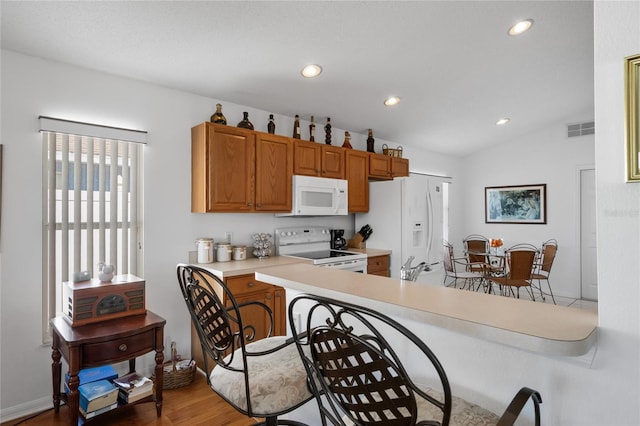 kitchen featuring hardwood / wood-style flooring, white appliances, kitchen peninsula, and vaulted ceiling