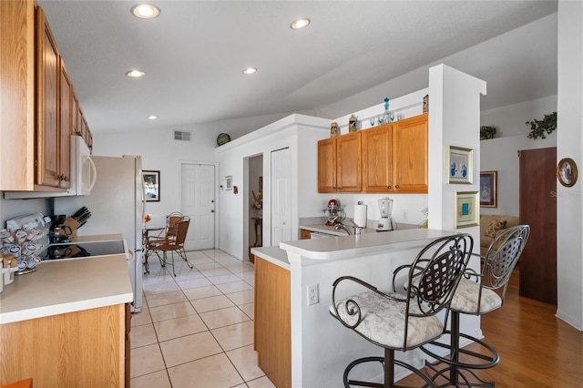 kitchen featuring kitchen peninsula, light tile patterned floors, lofted ceiling, and a breakfast bar area