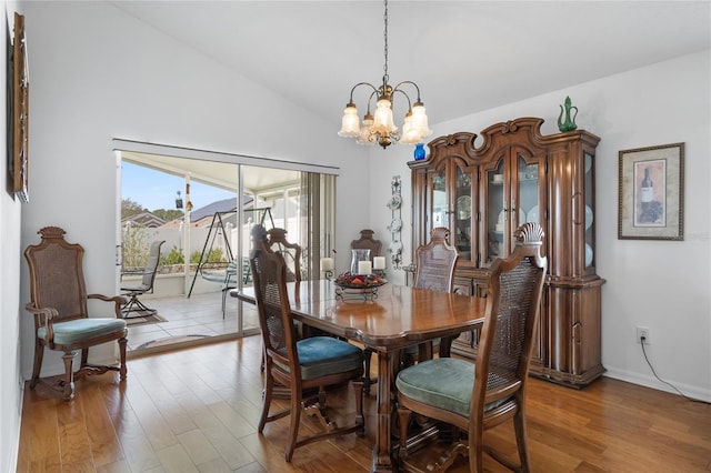 dining space with light wood-type flooring, an inviting chandelier, and vaulted ceiling