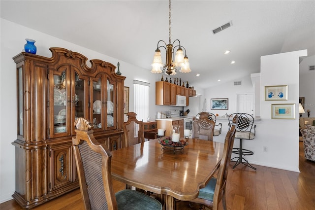 dining area with hardwood / wood-style floors, lofted ceiling, and a chandelier