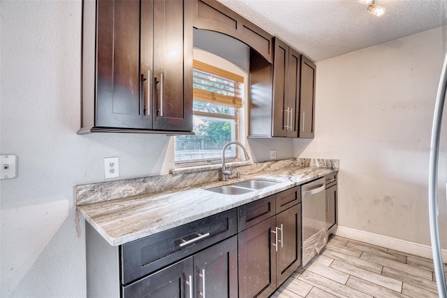 kitchen featuring dark brown cabinets, light stone counters, a textured ceiling, stainless steel dishwasher, and sink