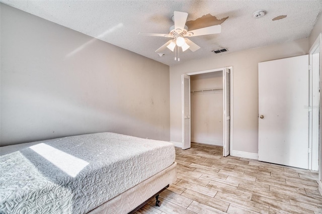 bedroom with light hardwood / wood-style flooring, a textured ceiling, a closet, and ceiling fan