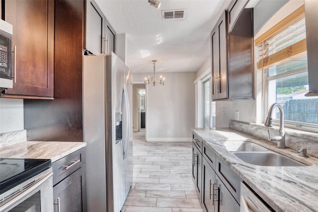 kitchen featuring appliances with stainless steel finishes, sink, light stone countertops, a textured ceiling, and light hardwood / wood-style flooring