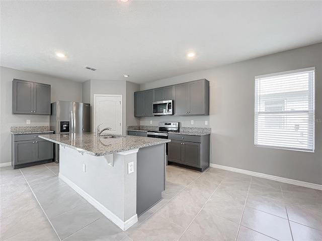 kitchen featuring an island with sink, stainless steel appliances, gray cabinetry, and a kitchen bar