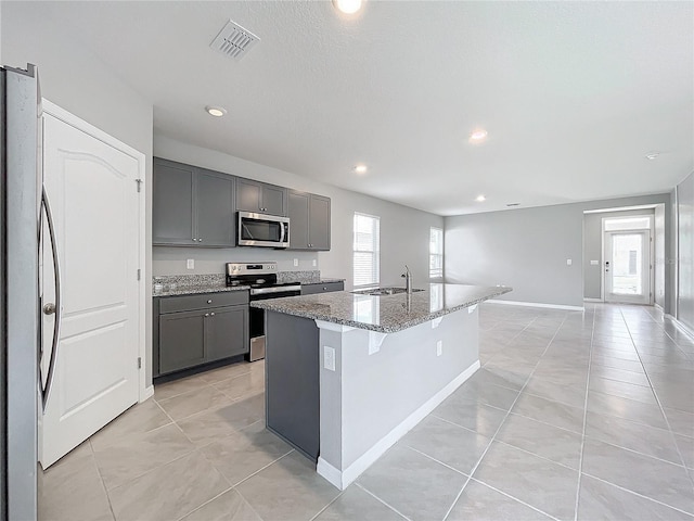 kitchen featuring gray cabinets, an island with sink, sink, and stainless steel appliances