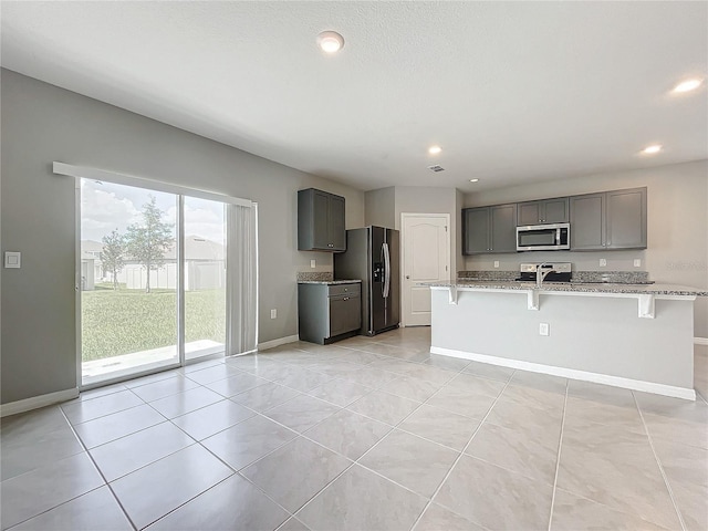 kitchen with light stone counters, an island with sink, appliances with stainless steel finishes, and a breakfast bar