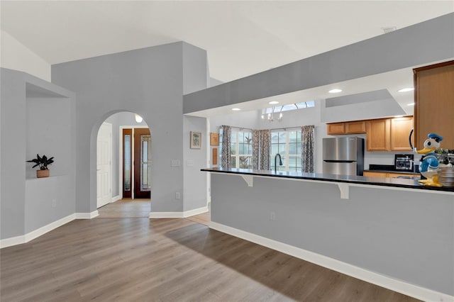 kitchen featuring sink, a kitchen breakfast bar, stainless steel fridge, light hardwood / wood-style flooring, and an inviting chandelier