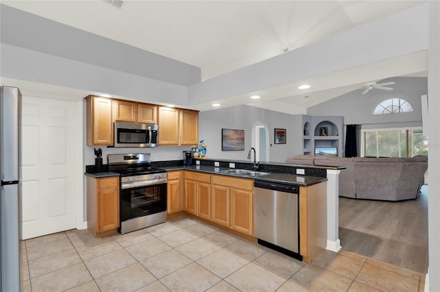 kitchen with light tile patterned floors, appliances with stainless steel finishes, dark stone counters, vaulted ceiling, and sink