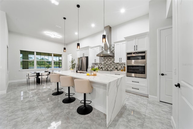 kitchen featuring white cabinets, wall chimney exhaust hood, pendant lighting, appliances with stainless steel finishes, and a center island with sink