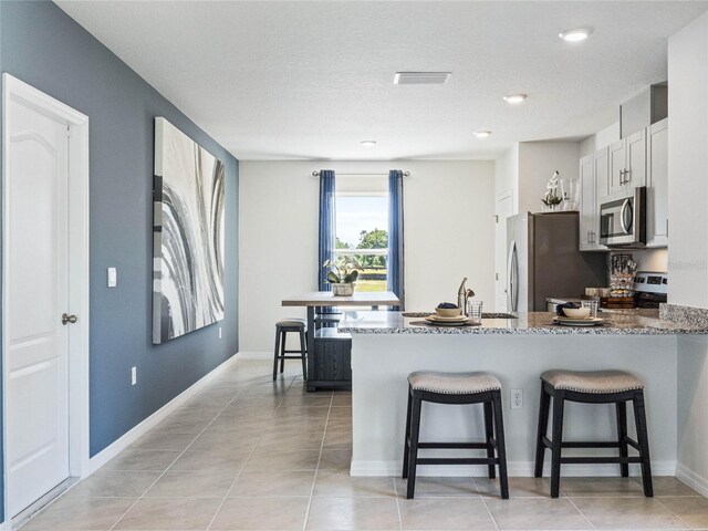 kitchen featuring white cabinetry, kitchen peninsula, a kitchen bar, stone counters, and appliances with stainless steel finishes