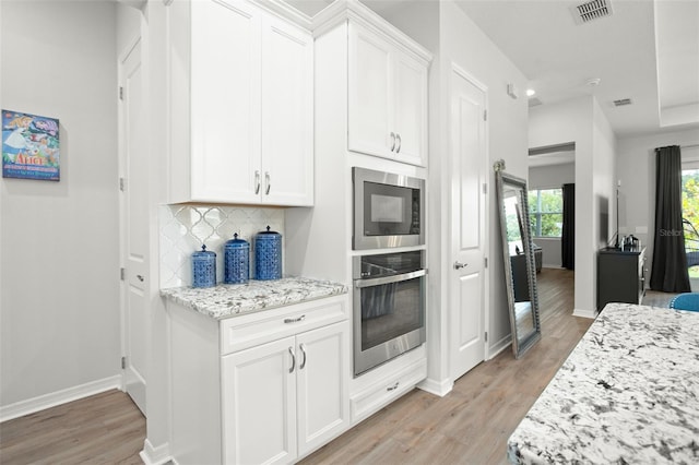 kitchen featuring tasteful backsplash, light wood-type flooring, white cabinetry, stainless steel appliances, and light stone counters