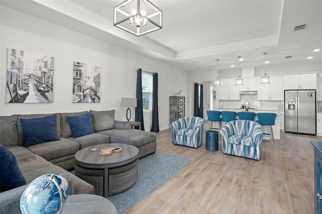 living room featuring light hardwood / wood-style floors, a notable chandelier, and a raised ceiling