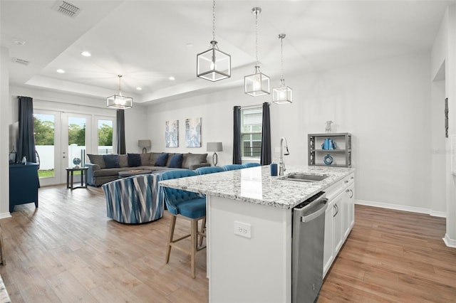 kitchen featuring dishwasher, an island with sink, light hardwood / wood-style flooring, decorative light fixtures, and white cabinetry