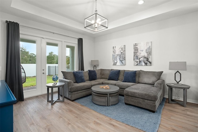 living room with wood-type flooring, an inviting chandelier, and a raised ceiling