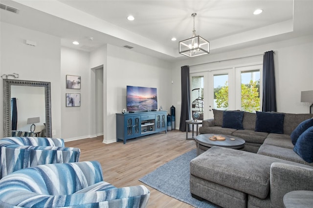 living room with a notable chandelier, a tray ceiling, and light wood-type flooring