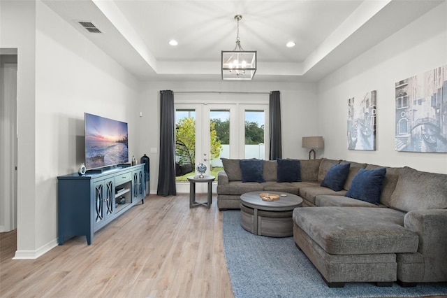 living room with french doors, light hardwood / wood-style floors, a notable chandelier, and a tray ceiling