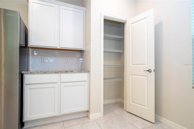 interior space with light tile patterned flooring, stainless steel fridge, backsplash, white cabinetry, and light stone countertops