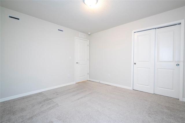 unfurnished bedroom with light carpet, a textured ceiling, and a closet