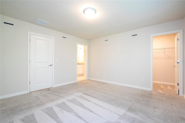 unfurnished bedroom with a spacious closet, a closet, light colored carpet, and a textured ceiling