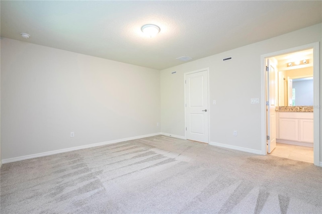 unfurnished bedroom featuring light carpet and ensuite bath