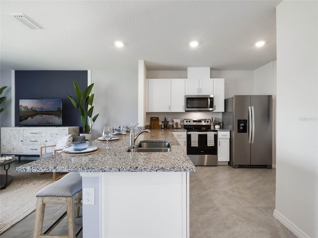 kitchen with white cabinetry, kitchen peninsula, light stone countertops, stainless steel appliances, and sink