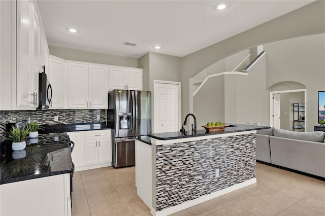 kitchen featuring white cabinets, light tile patterned floors, a kitchen island with sink, stainless steel fridge with ice dispenser, and dark stone counters