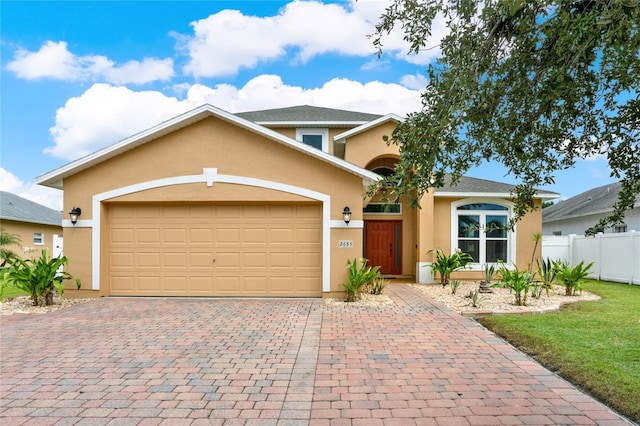 view of front of property with a garage, decorative driveway, fence, and stucco siding