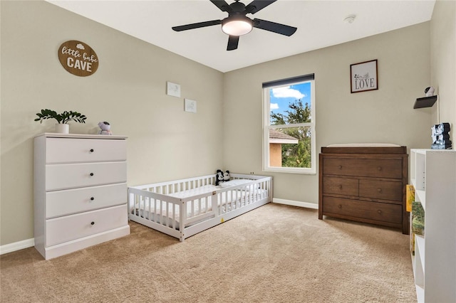 bedroom with a ceiling fan, a nursery area, light carpet, and baseboards