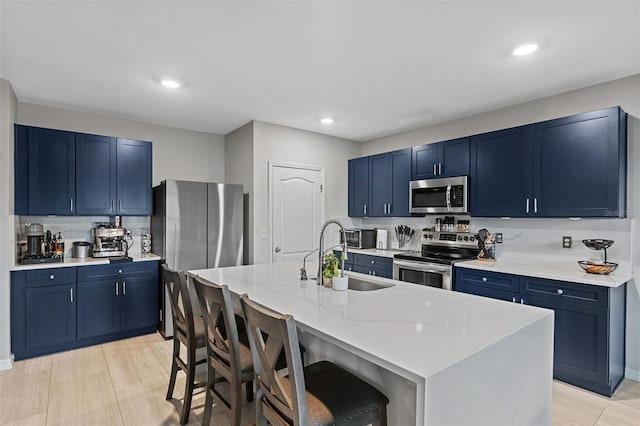 kitchen featuring appliances with stainless steel finishes, a kitchen breakfast bar, blue cabinetry, a center island with sink, and sink