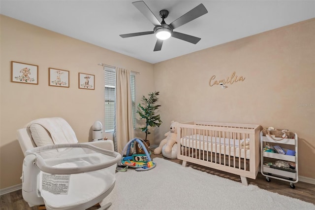 bedroom with a crib, dark hardwood / wood-style flooring, and ceiling fan