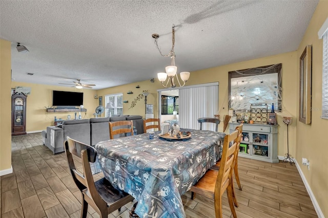 dining room featuring ceiling fan with notable chandelier, wood-type flooring, and a textured ceiling