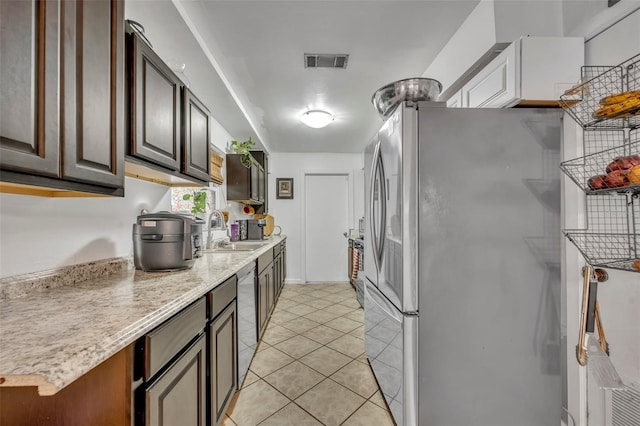 kitchen featuring dark brown cabinets, light tile patterned floors, stainless steel appliances, and sink