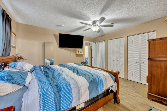 bedroom featuring ceiling fan, two closets, light hardwood / wood-style floors, and a textured ceiling