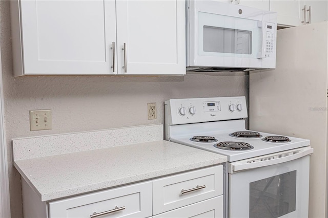 kitchen featuring white appliances, light stone countertops, and white cabinets